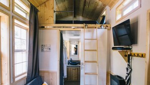 L’intérieur chaleureux d’un chalet avec un plafond en bois, un canapé avec des coussins, un téléviseur et une échelle.