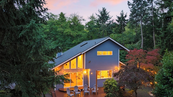 Une maison à deux étages avec une terrasse, entourée d’une forêt dense.