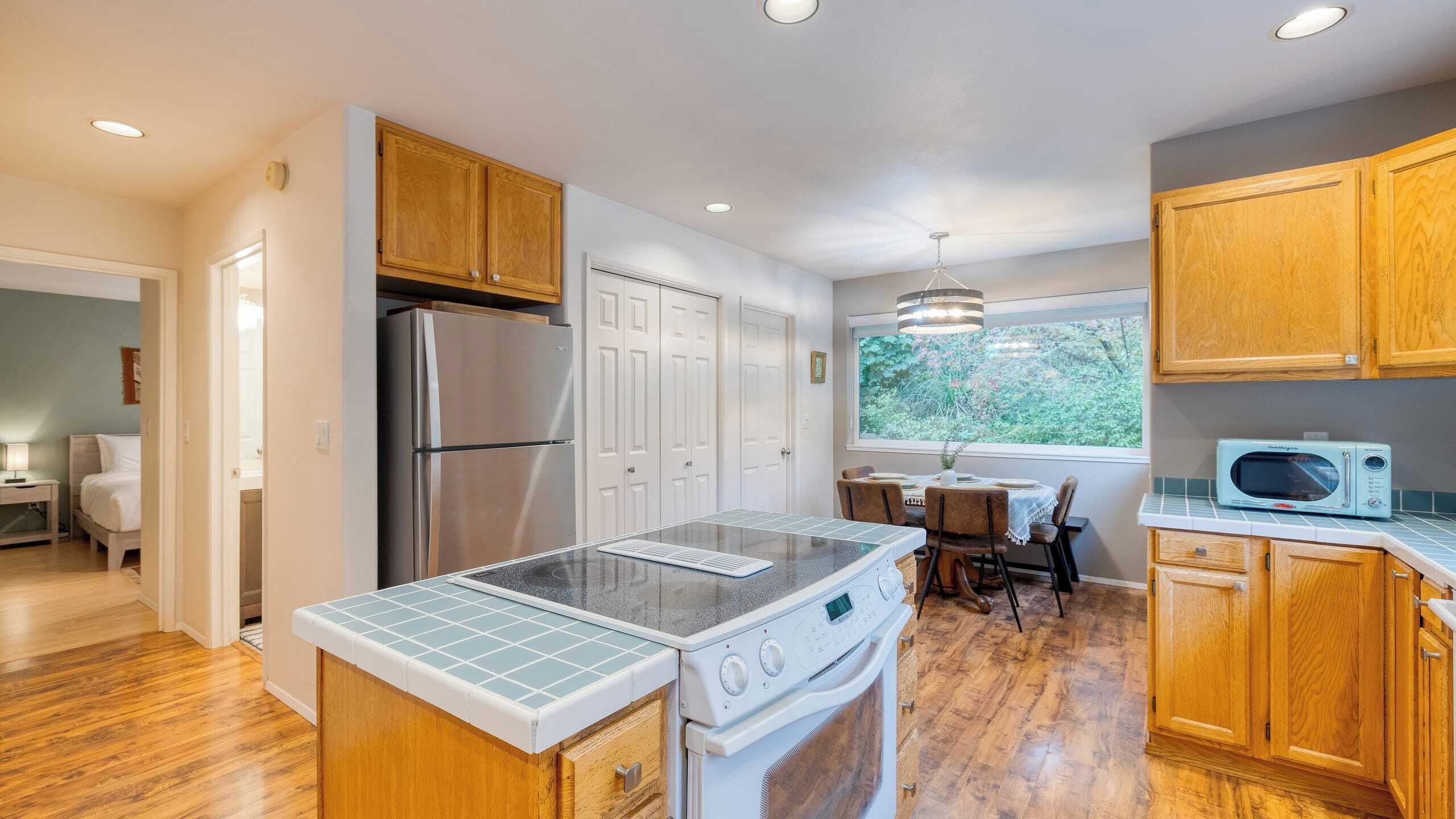 A modern kitchen with wooden cabinets, a stainless steel refrigerator, a built-in oven, and a microwave on the countertop.