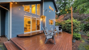 Une maison avec une terrasse, un espace salon extérieur et des guirlandes lumineuses.