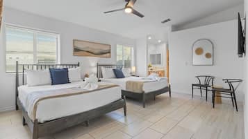 A hotel room with two beds, a ceiling fan, a bathroom with a mirror, and a small seating area.