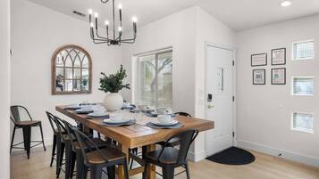 A dining area with a wooden table set for six, black chairs, a chandelier, a large mirror, and a potted plant.