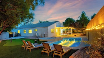 A backyard with a swimming pool, lounge chairs, and a covered patio area.