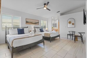 A hotel room with two beds, a ceiling fan, a bathroom with a mirror, and a small seating area.