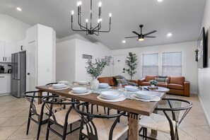 A modern kitchen with white cabinets, a dining table set for four, and a ceiling fan.