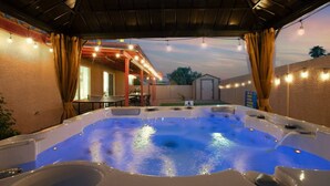 Zona de hidromasaje con techo cubierto, patio con mesa y sillas, y vista al jardín trasero.