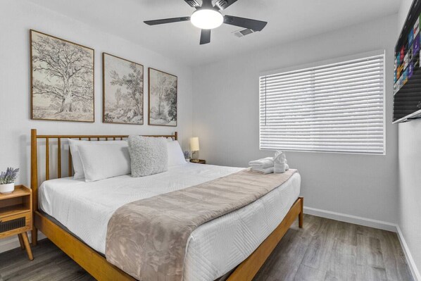A bedroom with a wooden bed, white bedding, a ceiling fan, and three framed artworks on the wall.