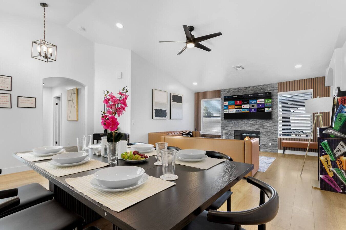A modern dining area with a long table set for four, a ceiling fan, and a mounted TV displaying various streaming services.