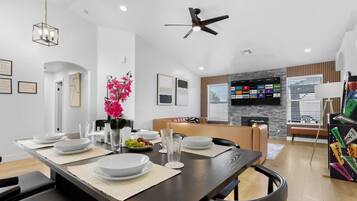A modern dining area with a long table set for four, a ceiling fan, and a mounted TV displaying various streaming services.