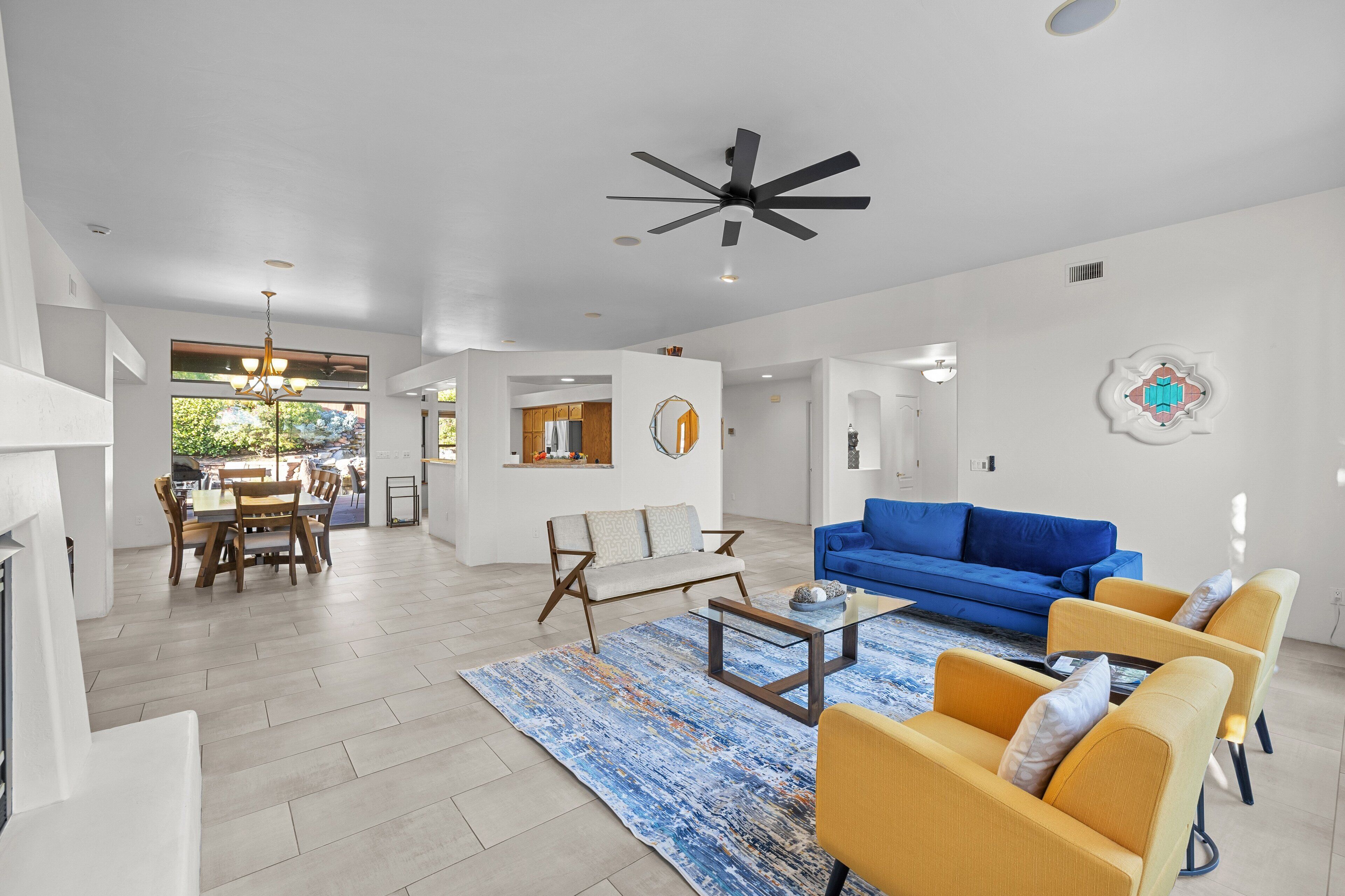 A spacious living area with a blue sofa, yellow armchairs, a coffee table, and a dining table with chairs.