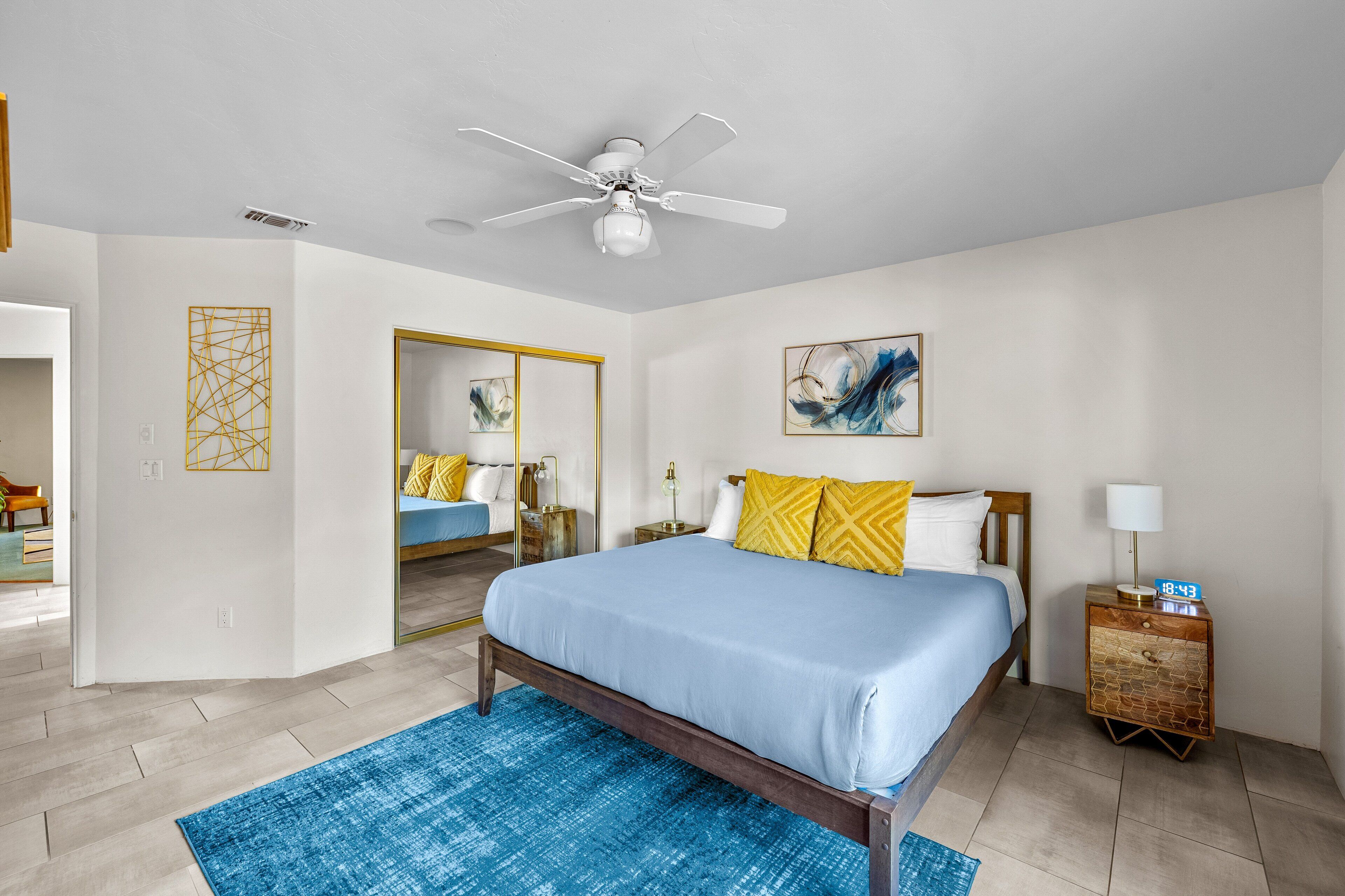A bedroom with a bed, a nightstand, a ceiling fan, and a painting on the wall.