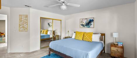 A bedroom with a bed, a nightstand, a ceiling fan, and a painting on the wall.