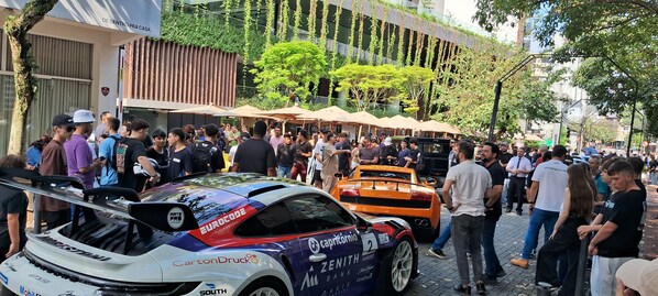A busy street with a rally car and a Lamborghini parked on the side.