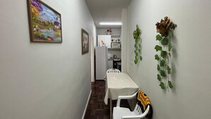 A narrow hallway with a dining table and chairs, a refrigerator, and a microwave in the background.