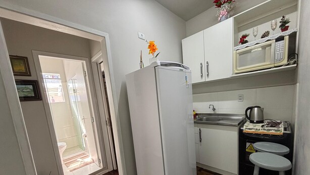 A compact kitchen with a refrigerator, a microwave, and a sink. There is a small stool and a potted plant.