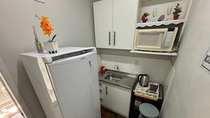 A compact kitchen with a white refrigerator, a microwave, a sink, and a small countertop with a kettle and a coffee machine.