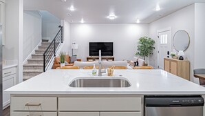 A modern kitchen with white cabinets, a stainless steel dishwasher, and a central island with a sink. - Brand New Townhome in proximity to the Hospital, Mall, Restaurants, and Parks. (Idaho Falls)