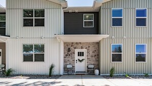A two-story building with a stone facade, a white door, and two chairs outside. - Brand New Townhome in proximity to the Hospital, Mall, Restaurants, and Parks. (Idaho Falls)