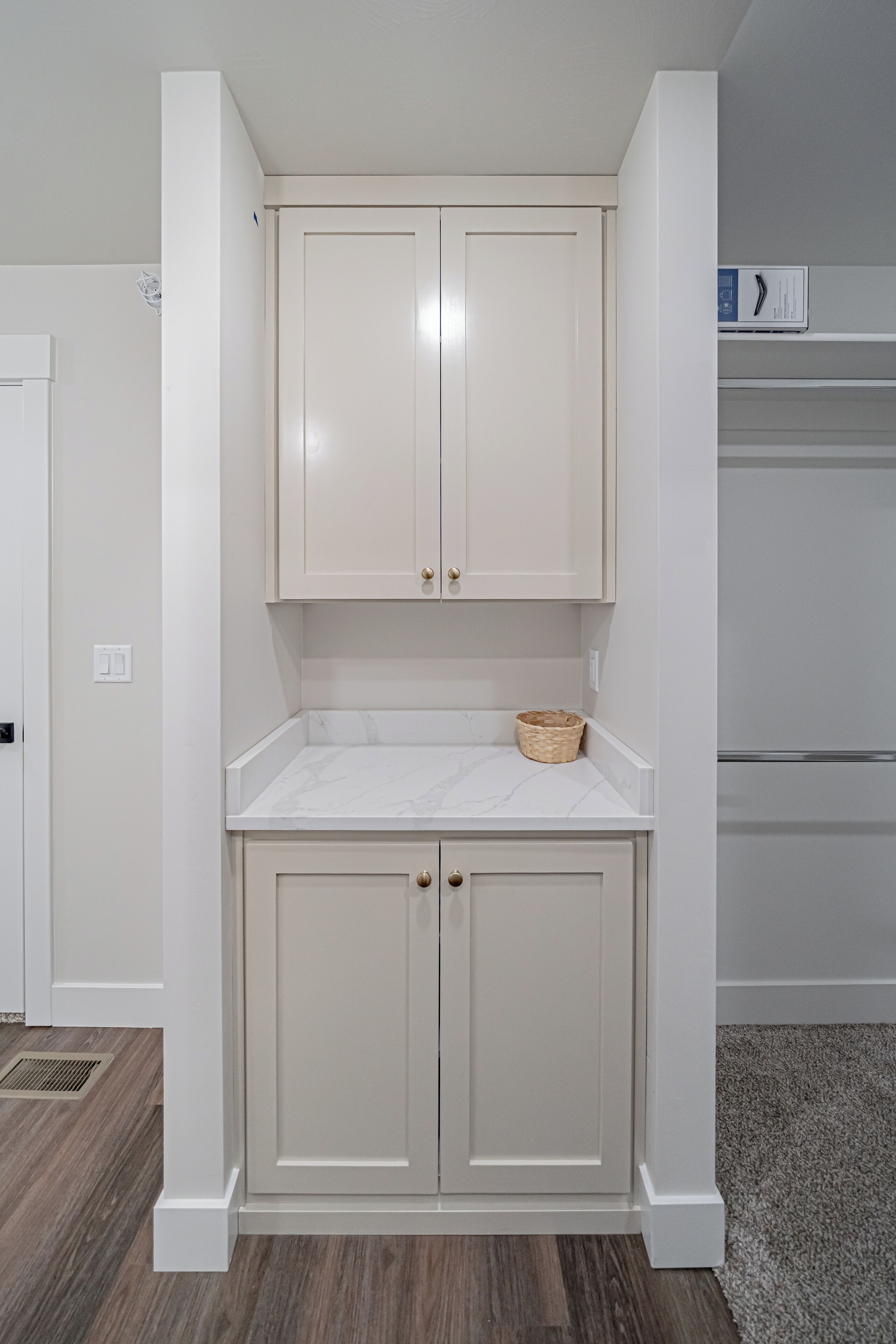 A compact kitchen with white cabinetry, a marble countertop, and a small woven basket.