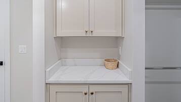 A compact kitchen with white cabinetry, a marble countertop, and a small woven basket.