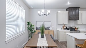 A modern kitchen with white cabinets, a wooden dining table, and a built-in island. - Brand New Townhome in proximity to the Hospital, Mall, Restaurants, and Parks. (Idaho Falls)