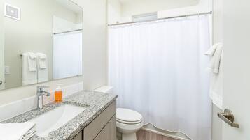 Une salle de bain moderne avec un lavabo sur un plan de travail en granit, des toilettes et une douche avec un rideau blanc.