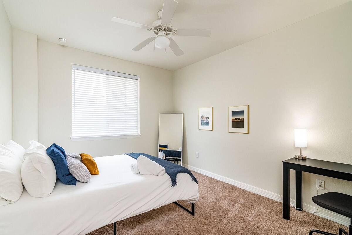 A bedroom with a bed, a ceiling fan, a desk, and a mirror.