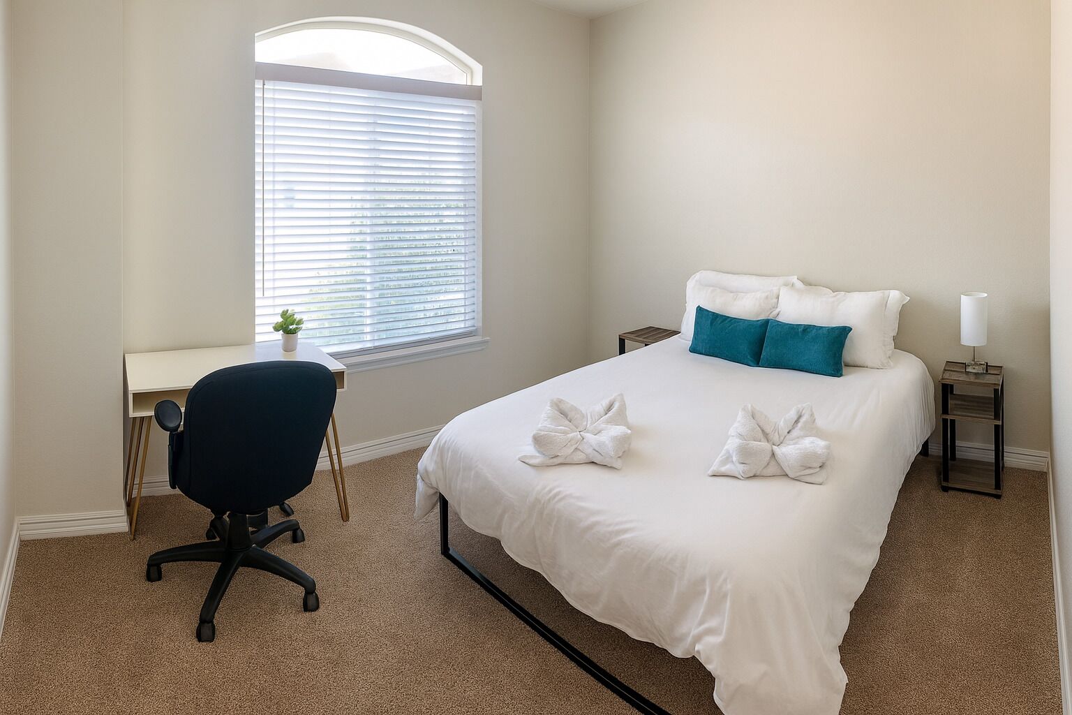 A bedroom with a bed, a desk, a chair, and a window with blinds.