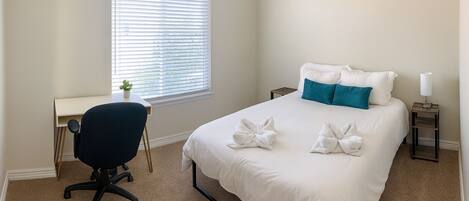 A bedroom with a bed, a desk, a chair, and a window with blinds.