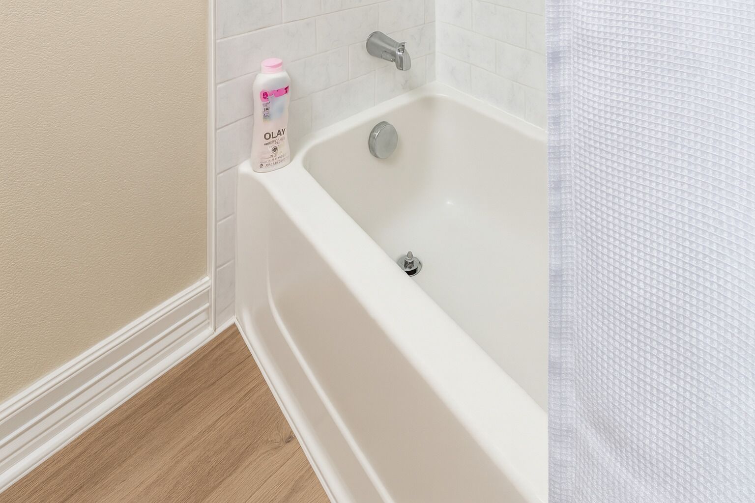 A bathroom with a white bathtub, a bottle of Olay shampoo, and a shower curtain.