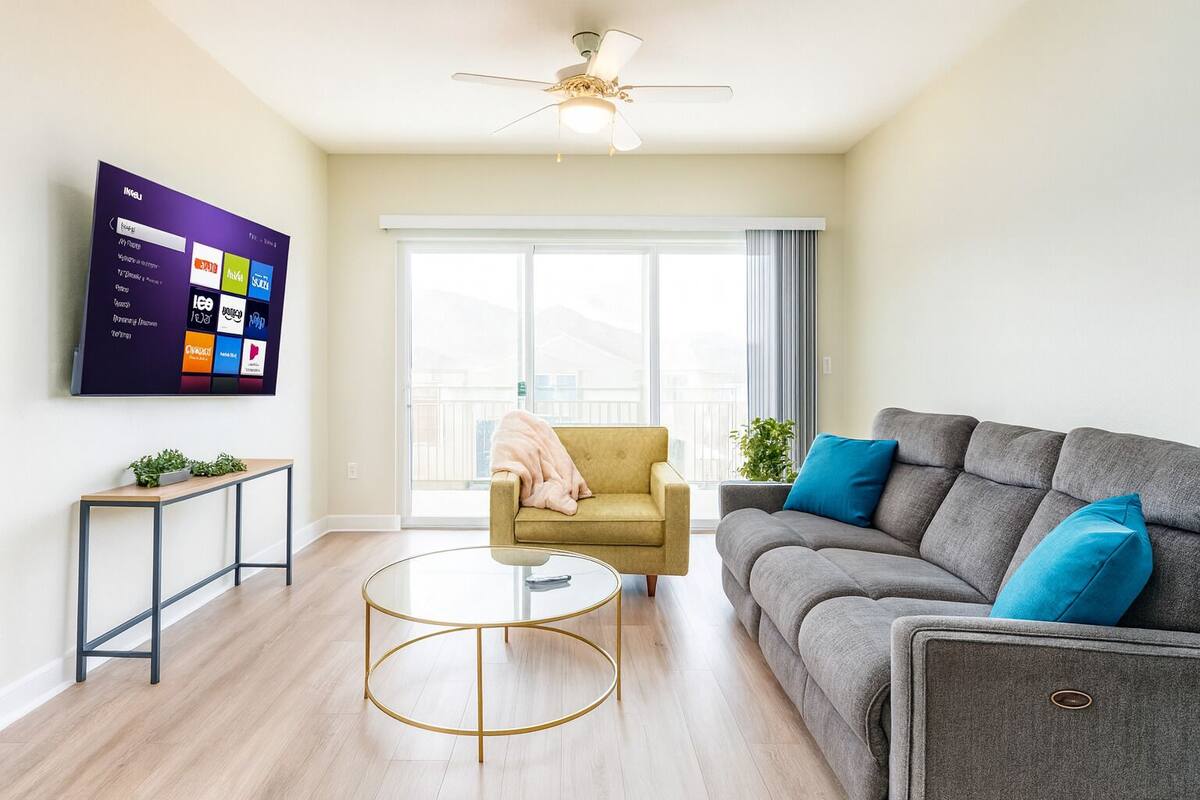 A modern living room with a sofa, armchair, coffee table, and a TV mounted on the wall.