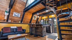 A cozy interior with a wooden bar area, a sofa with cushions, and a staircase. - Epic A Frame (Granite Falls)