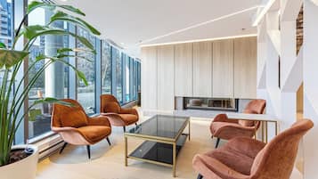 A modern living room with a glass coffee table, plush armchairs, and a fireplace.