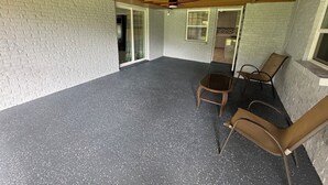 Un patio techado con suelo negro moteado, paredes de ladrillo blanco y vigas de madera en el techo.