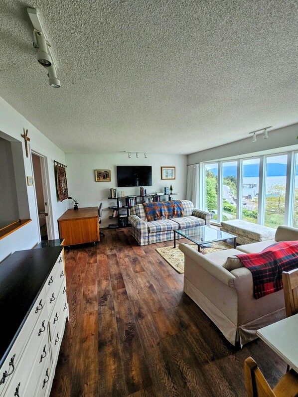 A living room with a sofa, a coffee table, a TV, and a view of the outdoors. - Piper's Bluff. Ocean view 3-bdrm, 2-bath apartment with weekly/monthly discounts (Daajing Giids)