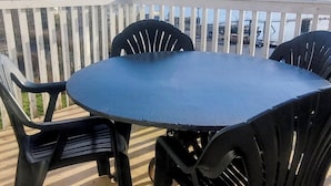En uteplats med ett bord och stolar, med utsikt över en sjö eller ett annat vattendrag och bortom det, mot avlägsna kullar.