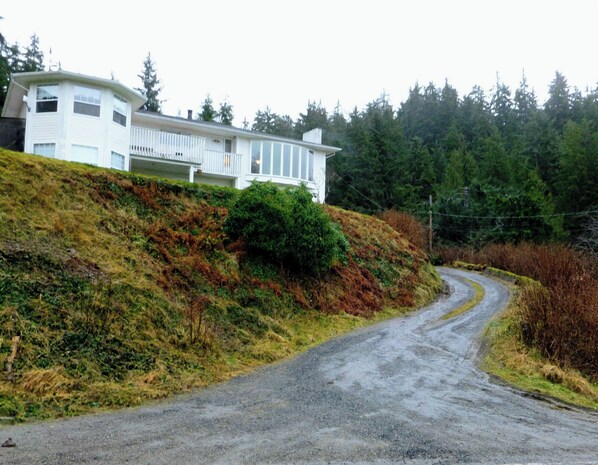 Una casa con techo inclinado y balcón, rodeada de un área boscosa y un camino sinuoso.