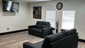 Een moderne woonkamer met een grote flatscreen televisie, twee zwarte banken, een houten visgraatvloer en een hangklok aan de muur.