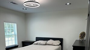 Een slaapkamer met een bed, nachtkastje, dressoir en een raam met jaloezieën.