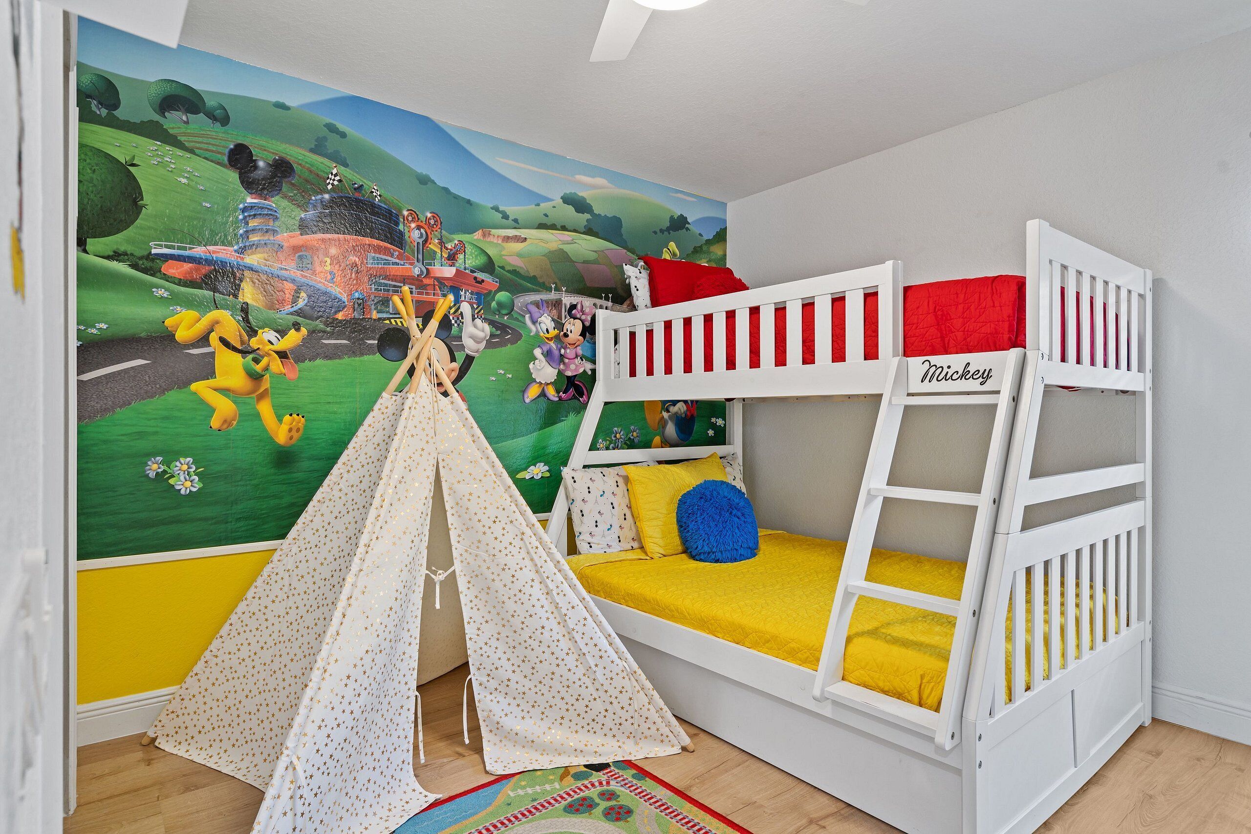 Ein Kinderstockbett mit Mickey Mouse Kopfstück, ein Spielzelt und eine Wandmalerei mit Zeichentrickfiguren.