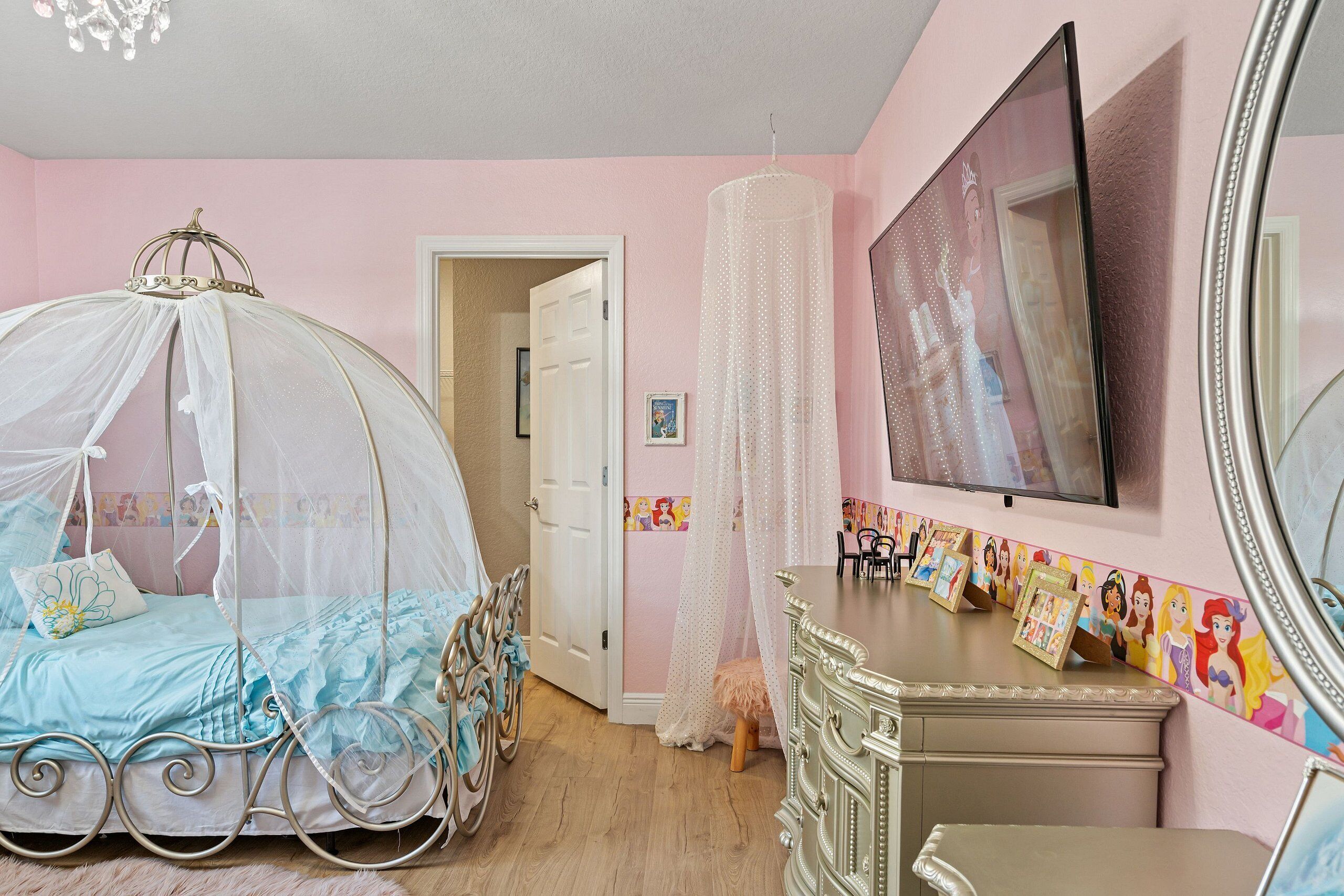 A bedroom with a canopy bed, a dresser, a mirror, and a wall with a Disney princess wallpaper.