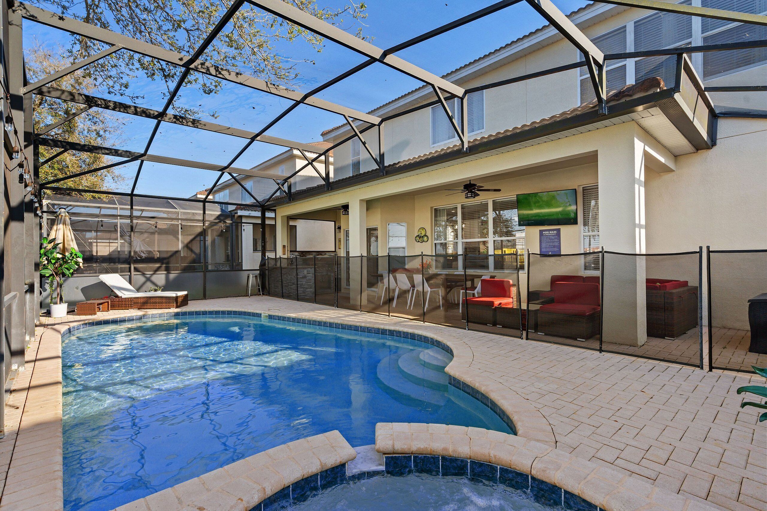 A swimming pool with a glass enclosure, lounge chairs, and a patio area with outdoor furniture.