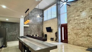 Una cocina amplia con una isla grande, un comedor con sofá, un televisor montado en la pared y un ventanal.