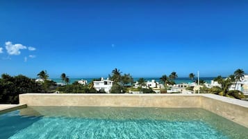 A clear blue sky, a swimming pool, and a view of the ocean and buildings.