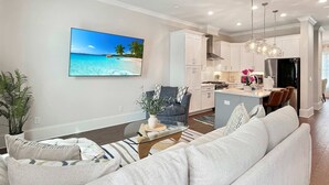 En moderne stue med en stor sofa, et sofabord og et fjernsyn, der viser et strandbillede.