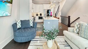 En moderne stue med sofa, sofabord med plante, og udsigt til køkken og spiseområde.