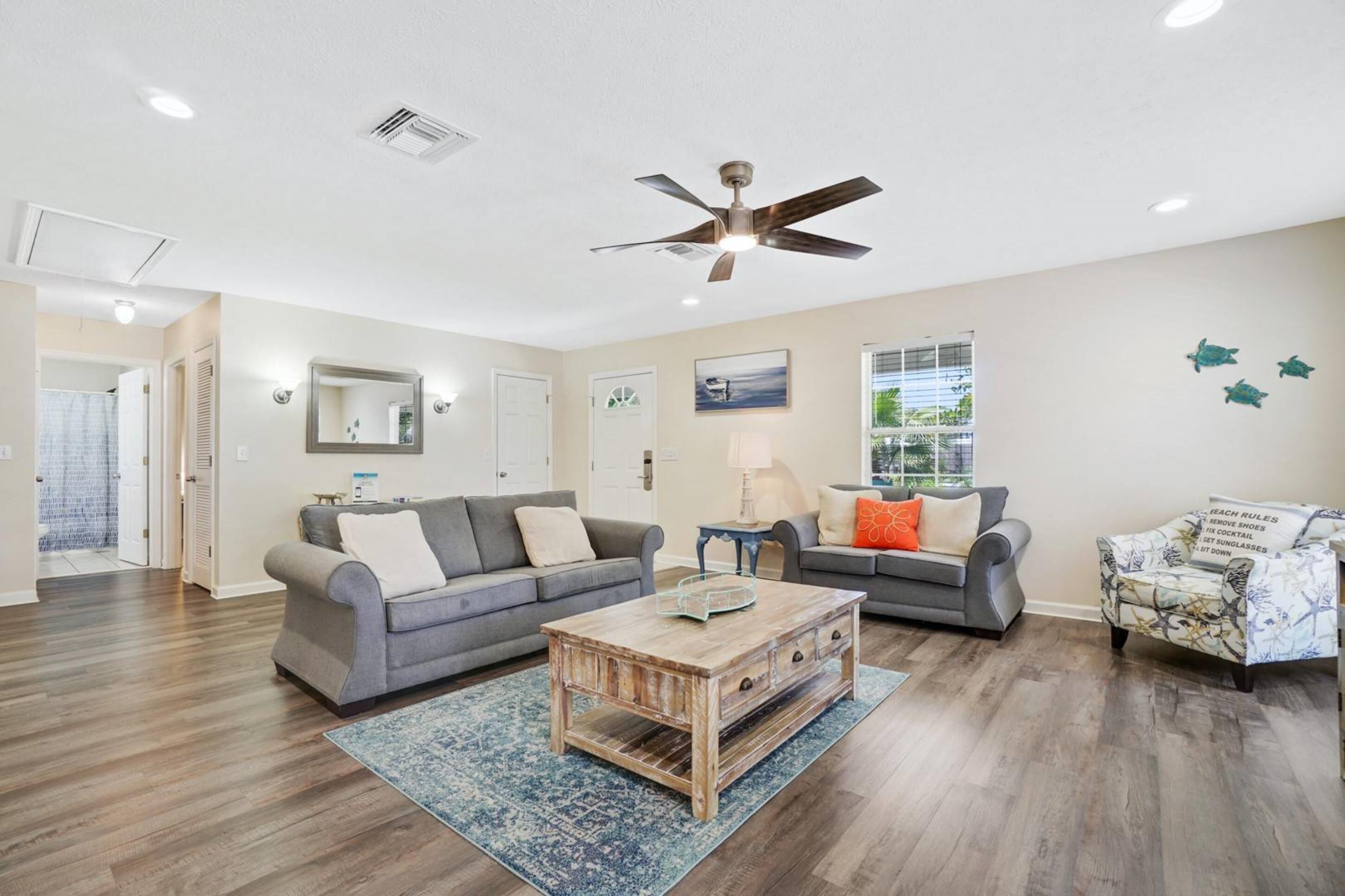 A spacious living room with two grey sofas, a wooden coffee table, and a ceiling fan.