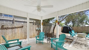 Ein überdachter Patio-Bereich mit türkisfarbenen Adirondack-Stühlen, einem Tisch und einem Deckenventilator.