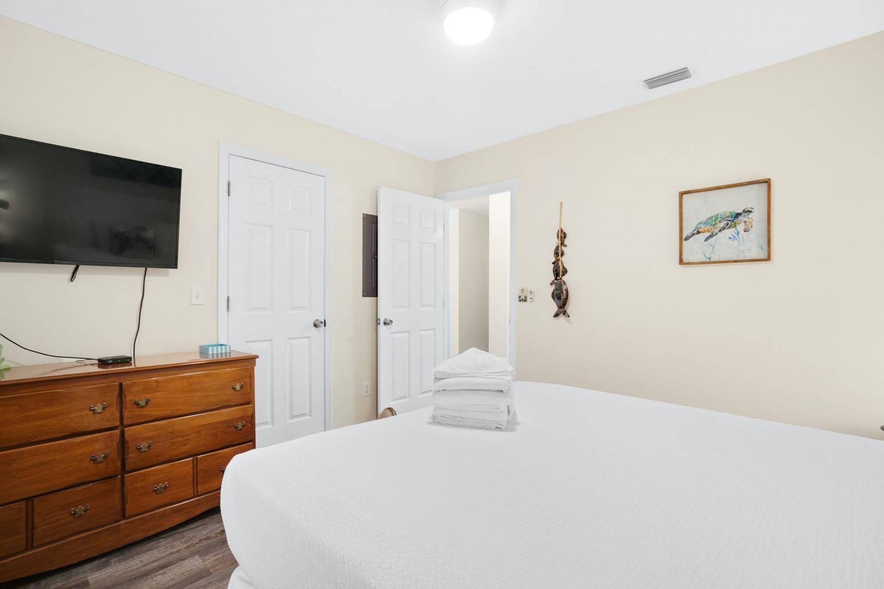 A hotel room with a large bed, a wooden dresser, a flat-screen TV, and a framed artwork on the wall.