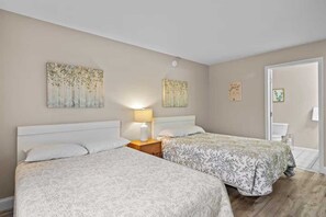 A hotel room with two beds, a nightstand with a lamp, and artwork on the walls. - 🛶 Torch Lake Vista – A-Ga-Ming Golf & Lakeview Condo | Large Patio  ➠ 741/Unit 9B (Kewadin)